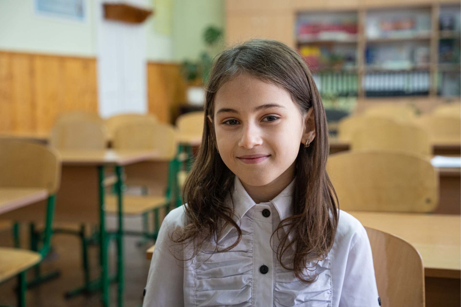 Ein Mädchen sitzt in einer Schule. Sie schaut direkt in die Kamera und lächelt.