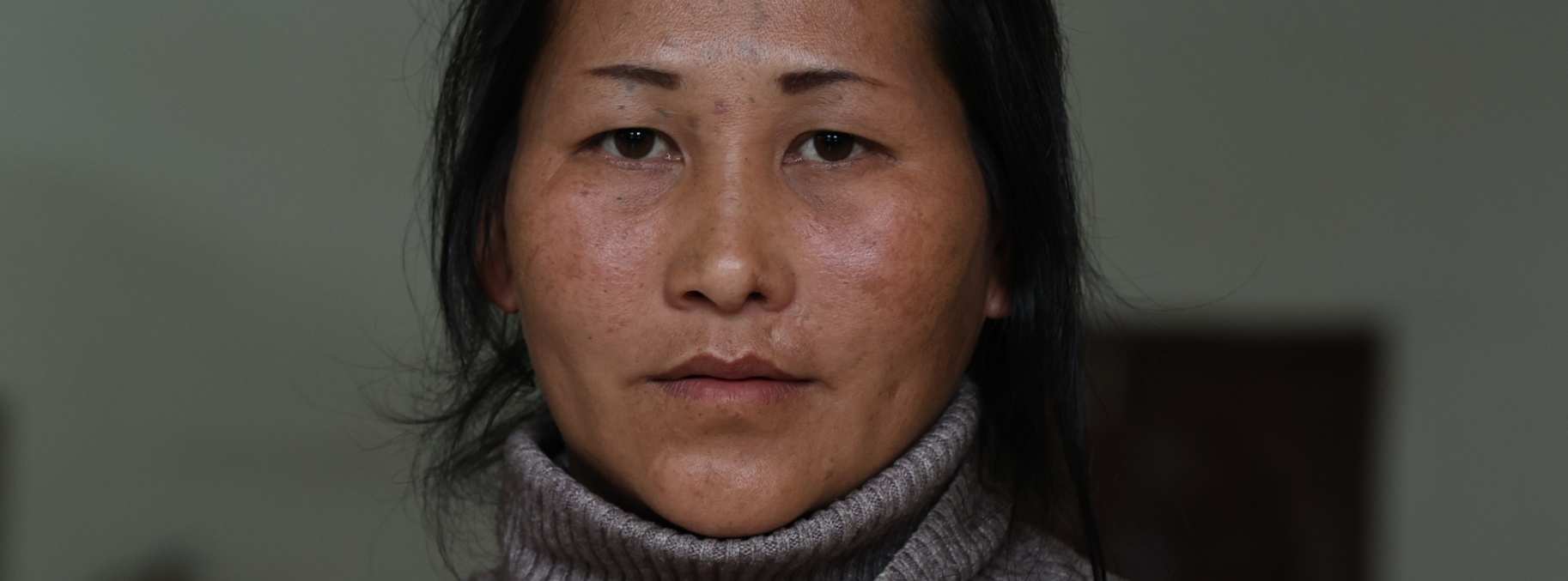 Portrait von Mrs Xoua, einer Frau mittleren Alters. Sie schaut neutral in die Kamera und hat den Kopf leicht geneigt.