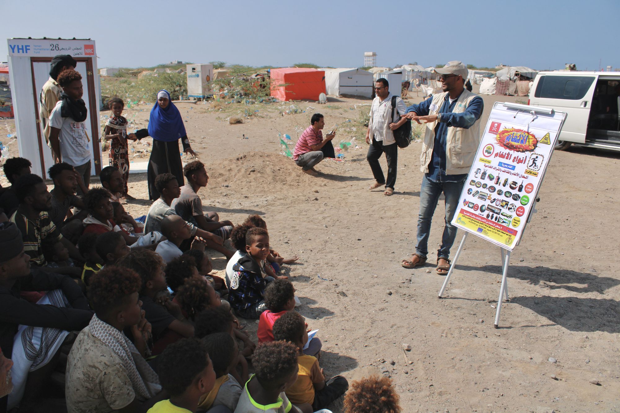Kinder und Jugendliche im Jemen hören einem HI-Mitarbeiter zu, der anhand einer Flipchart die Gefahren von Blindgängen erklärt Ein HI-Mitarbeiter erklärt einer Gruppe Menschen anhand von Infotafeln, wie sie sich vor Blindgängern schützen können.